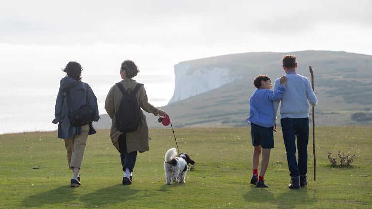 Three adults and a child walking on Tennyson Down, Isle of Wight, with a dog on a lead. Their backs are to the camera and they are walking into the distance.
